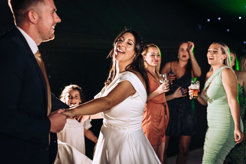 A Bride and Groom dance with their friends and children in a spotlighted room