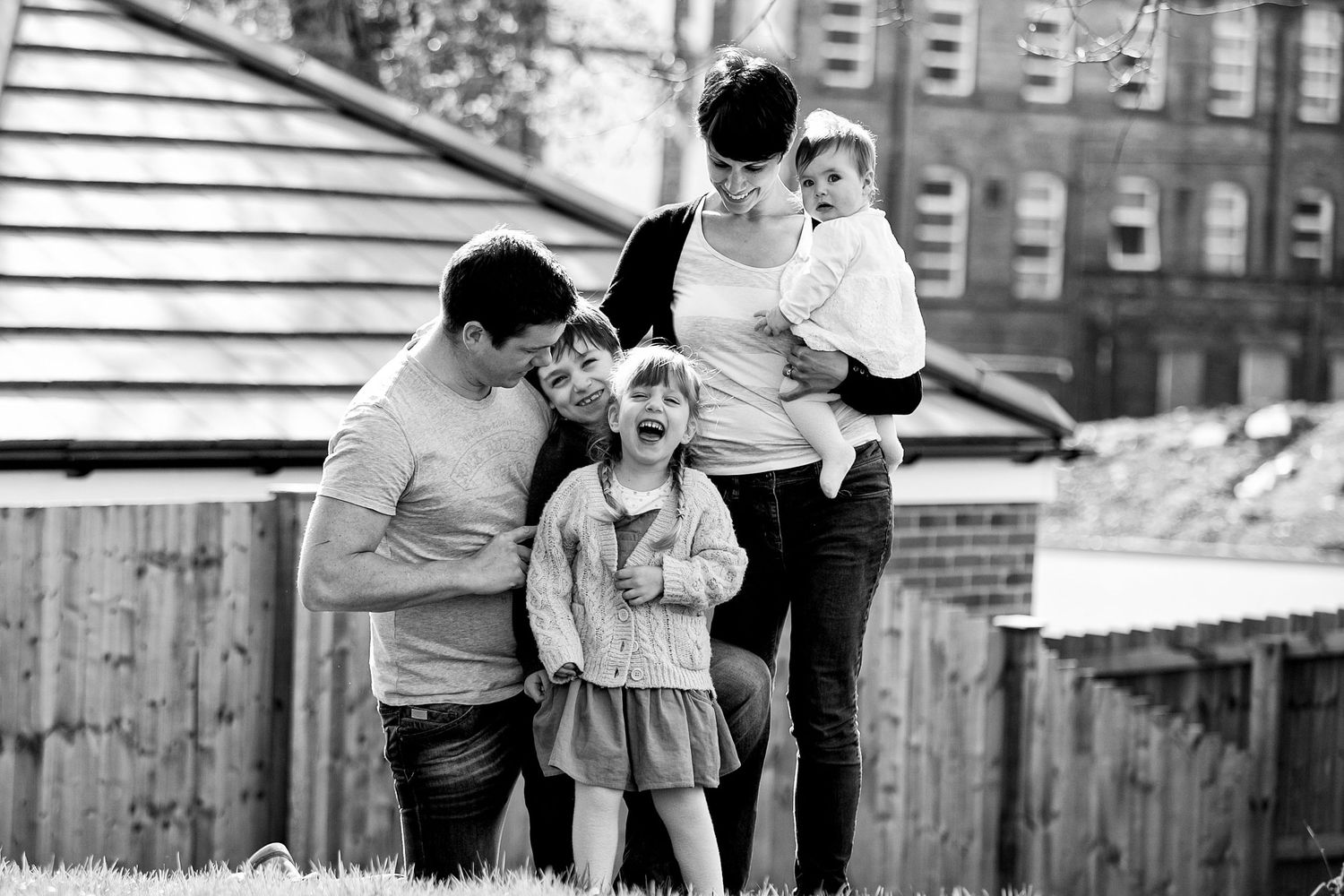 A father is surrounded by his family and tickles his daughter who laughs with delight