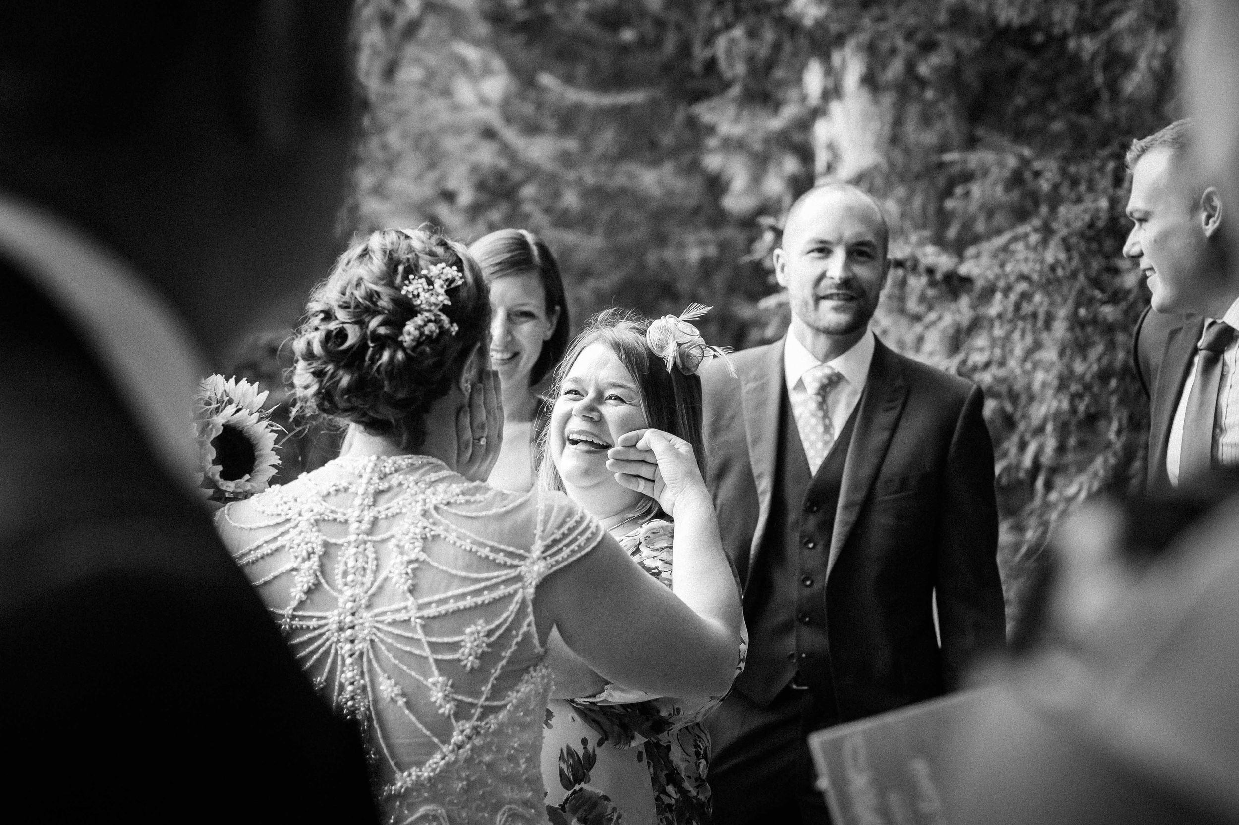 A bride gently brushes the face of her friend with the backs of her fingers as she gently cups the face of the bride