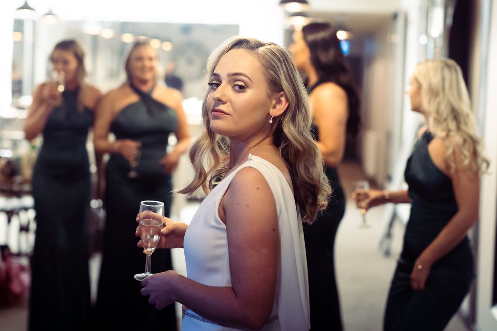 A bride is surrounded by four bridesmaids who talk together whilst she turns her head over her shoulder