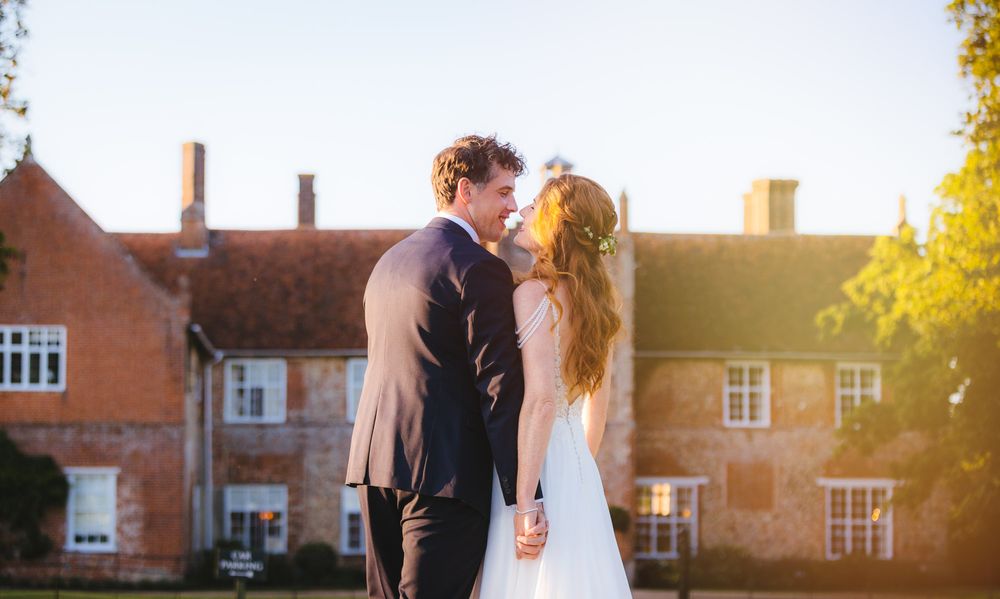 The Newly weds stand in front of Bruisyard Country Estate and look at each over lovingly on a sunny afternoon