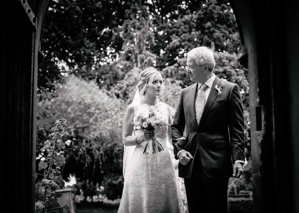 The Bride looks longingly at her father as they enter through the front doors of a church